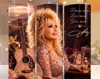 May include: A cylindrical tumbler featuring a portrait of Dolly Parton with blonde hair, an acoustic guitar, and floral arrangements. The text reads: Dream more, Love more, Give more, and Dolly. The design includes a sunset mountain landscape.