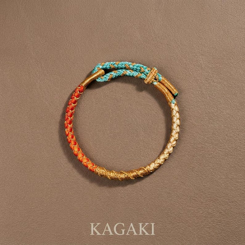 May include: A braided bracelet with sections of gold, orange, and turquoise. The bracelet is circular, with a clasp. The word "KAGAKI" is printed in white at the bottom of the image.