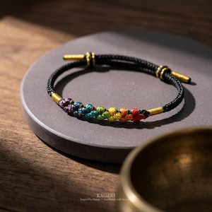 May include: A black bracelet with a rainbow flower design. The bracelet has gold-colored accents and is displayed on a gray surface. The bracelet is handmade and inspired by nature.