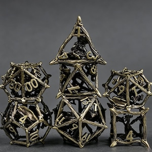 Könnte beinhalten: Satz antiker, messingfarbener Metalldürfel für Tischspiele. Die Würfel beinhalten einen D4, D6, D8, D10, D12, D20 und einen Prozentwürfel. Jeder Würfel hat ein offenes, käfigartiges Design mit sichtbaren Zahlen.