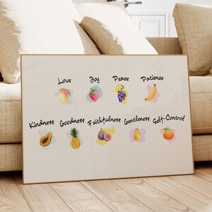 May include: A framed print featuring watercolor illustrations of fruits, each paired with a word: Love, Joy, Peace, Patience, Kindness, Goodness, Faithfulness, Gentleness, and Self-Control. The artwork is displayed in a living room setting.