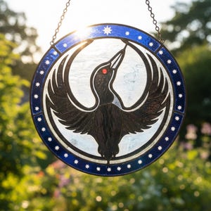 May include: A round stained glass window with a bird design. The bird is black with a red eye, set against a white background. The border is blue with white stars. The window hangs from a chain.