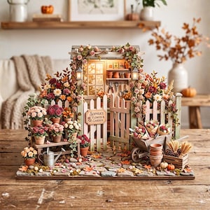 Könnte beinhalten: Eine Miniaturgartenszene mit einem Holztor und einem Schild mit der Aufschrift Sophia's Flower & Garden, umgeben von Topfblumen, Kletterrosen, einer Schubkarre, einer Holzkiste mit Weizen, einer Metallgießkanne und einem gepflasterten Weg.