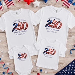 Puede incluir: Camisetas blancas y un body para bebé con diseño patriótico. Las camisetas y el body muestran el texto "SIMMON'S FAMILY 250 Years of Freedom BOSTON, MA" en rojo, blanco y azul. Ideal para una celebración familiar.