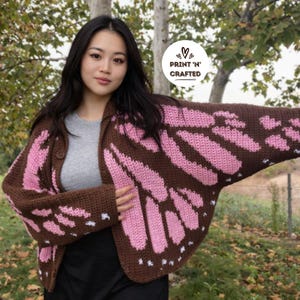 May include: A brown and pink crochet cardigan with a butterfly wing design. The open-front sweater features a button closure and white accents. The image includes the text "PRINT 'N' CRAFTED" in a circular logo.