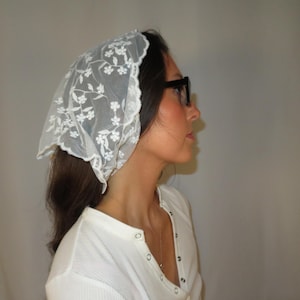 Puede incluir: Un pañuelo de encaje blanco con un diseño floral. El pañuelo se lleva en la cabeza. La persona lleva una camisa blanca y gafas negras. El pañuelo es de estilo vintage.