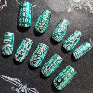 May include: A set of ten press-on nails featuring a metallic emerald green base with silver circuit board patterns and binary code designs. Each nail has a rectangular shape with rounded edges, displaying intricate lines and numeric sequences.