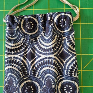 May include: A small, square drawstring bag with a repeating pattern of navy blue and white circular and diamond shapes. The bag has a silver-colored drawstring closure.
