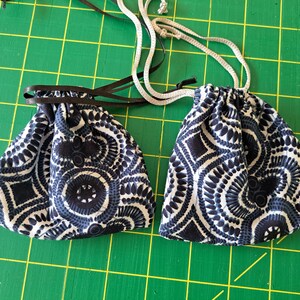 May include: Two small drawstring pouches with a navy blue and white circular pattern. One has a black drawstring, the other has a white drawstring. The pouches are on a green grid surface.
