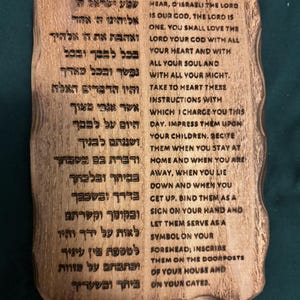 May include: A wooden plaque with engraved text in Hebrew and English. The plaque has a natural wood grain finish and a rustic, irregular shape. The text is a religious passage, likely a prayer or scripture.