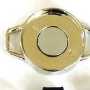 May include: A silver-toned key chain with a round, flat, circular disc in the center. The disc has a smaller, round, silver-toned disc in the center.