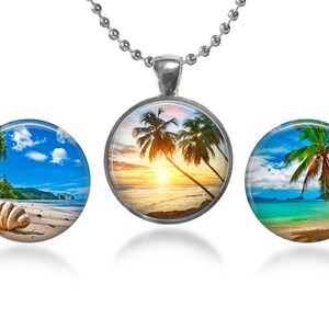 May include: Three round glass pendants with silver chains, each featuring a different tropical beach scene. The first pendant shows a beach with palm trees, a seashell, and blue water. The second pendant shows a sunset over the ocean with palm trees. The third pendant shows a palm tree on a beach with turquoise water.