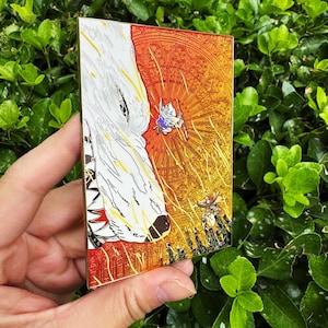 May include: A rectangular enamel pin featuring a detailed illustration. The design includes a white wolf's head on the left and a vibrant, detailed scene on the right with figures and a sunburst background. The pin has a gold border.