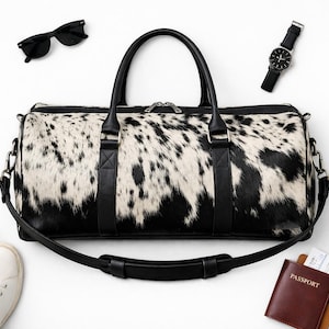 May include: A black and white cowhide duffel bag with black leather handles and a detachable shoulder strap. The bag is surrounded by white trainers, black sunglasses, a wristwatch, a brown passport holder, a small black bottle, and a camera.