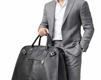 May include: A black leather travel bag with a zip closure and white stitching is held by a person wearing a grey suit and white shirt. The bag has two handles and a shoulder strap. The person is standing against a white background.