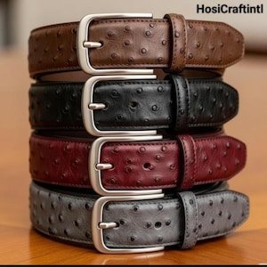 Puede incluir: Una pila de cuatro cinturones de cuero en marrón, negro, burdeos y gris. Cada cinturón tiene una hebilla plateada y una superficie texturizada con pequeños puntos espaciados. Un accesorio de moda.