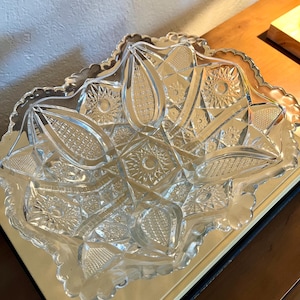 May include: A clear, decorative glass serving dish with a scalloped edge. The dish features a detailed, geometric pattern with starburst and diamond shapes. The dish is designed to hold food items and is suitable for entertaining.