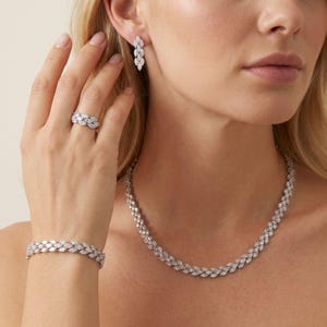 May include: A jewelry set consisting of a necklace, a bracelet, a ring, and drop earrings, all featuring a repeating marquise-cut stone pattern in a silver-toned metal setting. The pieces are coordinated with a consistent leaf-like design.