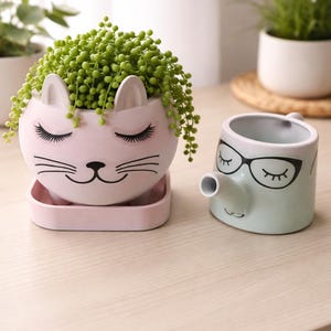 May include: A set of three ceramic mugs with a speckled, matte finish. The mugs are in shades of cream, light gray, and dark gray. Each mug has a simple, minimalist design and a rounded handle.