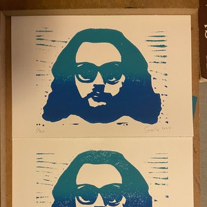 May include: Two framed prints of a blue and green silhouette of a person wearing sunglasses. The prints are numbered 1/20 and 2/20 and signed "Sawlle 2024".