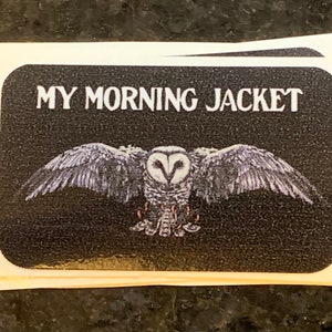 May include: A stack of stickers with a black background and the text "MY MORNING JACKET" in white. Below the text is a detailed illustration of an owl with outstretched wings.