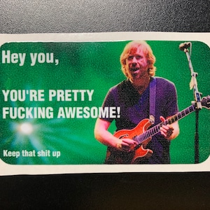 May include: A green and white sticker with a picture of a man playing a guitar. The text on the sticker reads "Hey you, YOU'RE PRETTY FUCKING AWESOME! Keep that shit up."