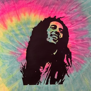 May include: A tie-dye t-shirt featuring a black silhouette of Bob Marley on the front. The shirt is a light blue, yellow, pink, and green colour.
