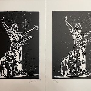 May include: Two black and white linocut prints of a person with a guitar standing on a dog. The prints are numbered 1/20 and 2/20 and signed "Sauille 2023".