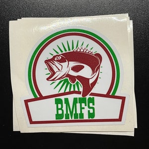 May include: A white sticker with a green and red circle containing a red bass fish with a white mouth and green rays. The text "BMFS" is written in green letters on a red banner below the circle.