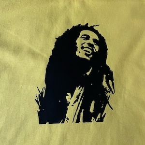 May include: A yellow t-shirt featuring a black silhouette of Bob Marley on the front.
