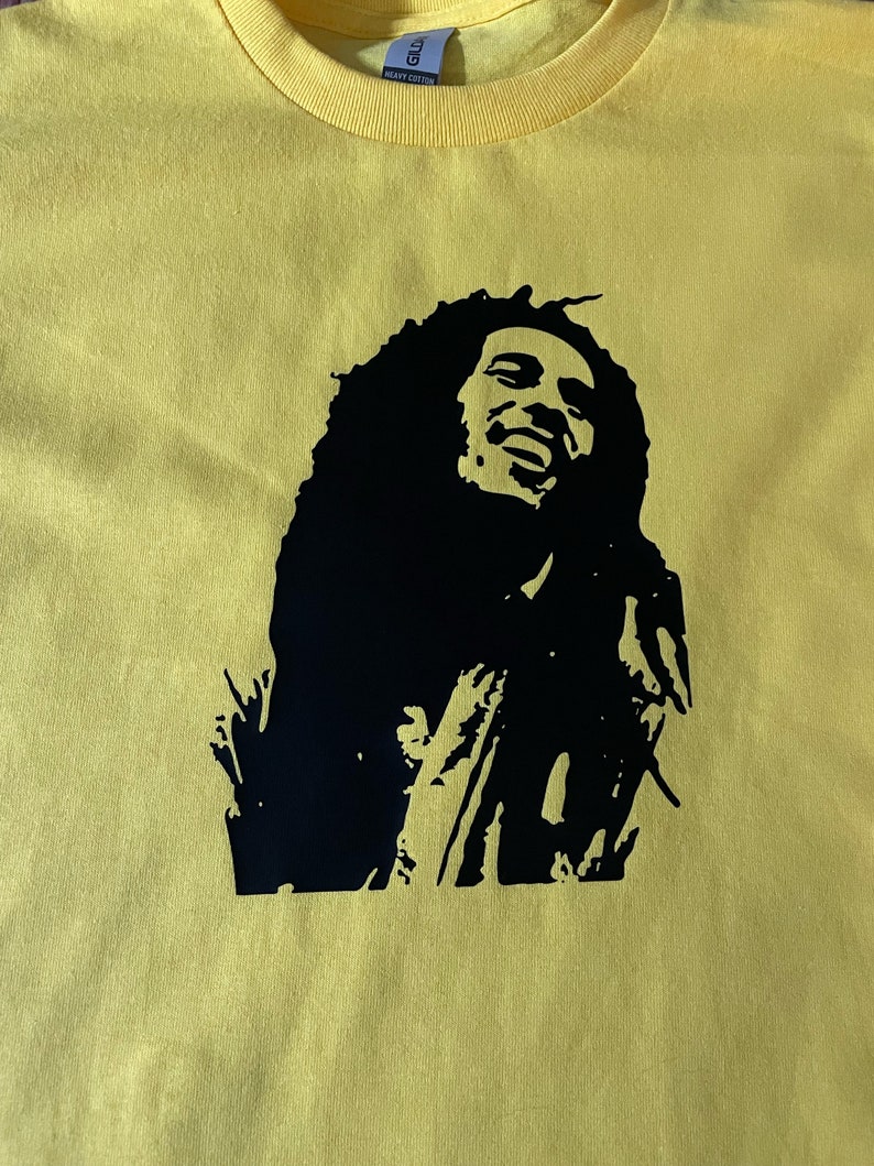 May include: A yellow t-shirt featuring a black silhouette of Bob Marley on the front.