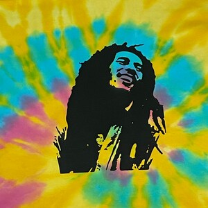 May include: A yellow, blue and pink tie-dye t-shirt featuring a black silhouette of Bob Marley singing.