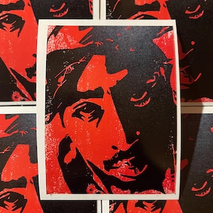 May include: A close-up of a red and black print of a person's face. The print is on a white background and has a distressed look.