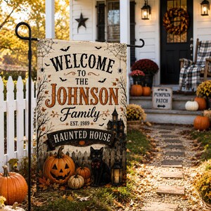 Könnte beinhalten: Eine rechteckige Gartenflagge mit cremefarbenem Hintergrund und schwarzem Text, der Welcome to the Johnson Family Est. 1989 Haunted House lautet. Das Design zeigt eine schwarze Katze, orangefarbene Kürbisse, ein Spukhaus, Spinnweben und Fledermäuse.