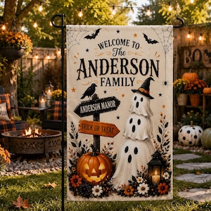 Op de afbeelding: Een rechthoekige tuin vlag met een crèmekleurige achtergrond, drie gestapelde witte geesten, een uitgesneden oranje pompoen en een zwarte lantaarn. De tekst luidt Welcome to The Anderson Family, Anderson Manor en Trick or Treat.
