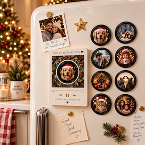 May include: A collection of magnetic photo frames and a rectangular magnetic plaque on a refrigerator. The plaque features a golden retriever in a wreath, the text 'OUR CHRISTMAS 2026', and 'HOME FOR CHRISTMAS'. Eight circular magnets display various holiday photos.