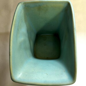 May include: A square turquoise ceramic vase with rounded corners. The interior is a darker shade of turquoise. The vase has a smooth, glossy finish and appears handmade. The design is simple and modern. The vase is approximately 15 cm tall.
