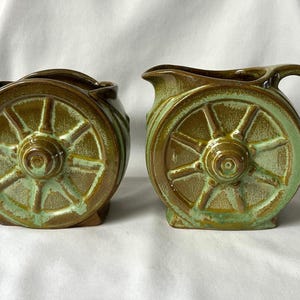 Pode incluir: Uma caneca de cerâmica branca com uma alça preta e o texto "But First, Coffee" em estilo manuscrito. A caneca está sobre uma superfície branca. A caneca tem aproximadamente 10 cm de altura.