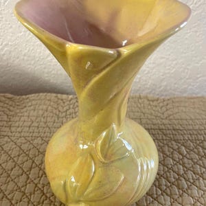 May include: A yellow ceramic vase with a flared top and a bulbous base. The interior of the vase is a soft pink. The exterior features a leaf design and a textured finish. The vase is likely for decorative purposes.