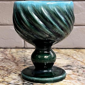 Peut inclure: Un calice en céramique présentant un émail vert forêt profond et turquoise avec une texture nervurée en spirale sur le bol. Le récipient possède une tige arrondie lisse et une large base circulaire, le tout avec une finition brillante.