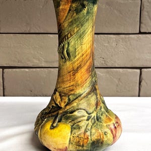 May include: A hand-painted ceramic vase with a bulbous base and a slender neck. The vase features a textured surface with a blend of colors, including yellow, green, and orange. The design incorporates leaf and vine motifs.