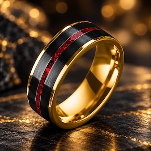 May include: A gold-toned ring featuring a wide, brushed black center band with a thin, vibrant red inlay running horizontally through the middle. The edges of the ring are polished gold, creating a high-contrast look with the dark center.