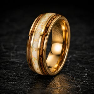 May include: A gold-toned ring featuring a central inlay of white crushed opal with gold flecks, flanked by two bands of dark brown wood grain. The ring has a polished metallic finish and a smooth, rounded profile with a reflective inner surface.