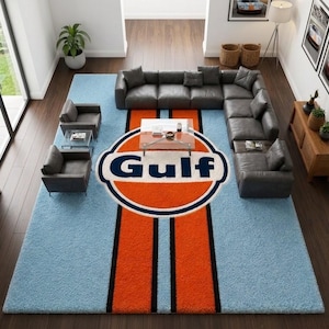 Può includere: Un grande tappeto rettangolare che presenta l'iconico logo Gulf Oil al centro con un emblema circolare arancione, testo blu scuro e due strisce verticali arancioni bordate da sottili linee nere su uno sfondo azzurro testurizzato.