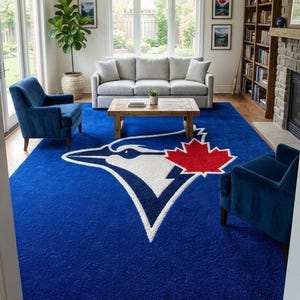 Peut inclure: Un grand tapis rectangulaire arborant le logo des Blue Jays de Toronto au centre. Le tapis est bleu profond avec une silhouette d'oiseau blanche et une feuille d'érable rouge proéminente. La surface texturée recouvre le sol du salon.