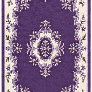 May include: A rectangular area rug featuring a deep purple center with a central cream-colored medallion. The border displays intricate scrolling floral patterns in shades of purple, lavender, and green against a cream background.