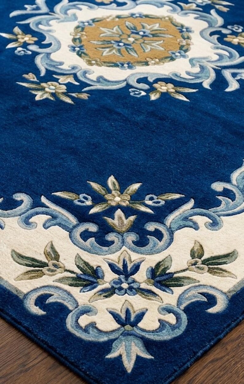 May include: A rectangular area rug featuring a deep blue background with a central tan medallion surrounded by cream-colored borders. The design includes intricate floral motifs and scrolling leaf patterns in shades of light blue, sage green, and white.