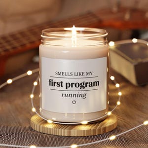 Puede incluir: Una taza de cerámica blanca con un asa negra y el texto "But First, Coffee" en negrita negra. La taza está sobre una superficie de madera. La taza mide 10 cm de alto.