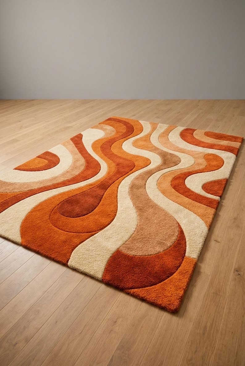 May include: A rectangular rug with a retro design. The rug features a wavy pattern in shades of orange, cream, and brown. The rug is placed on a wooden floor, creating a warm and inviting atmosphere.