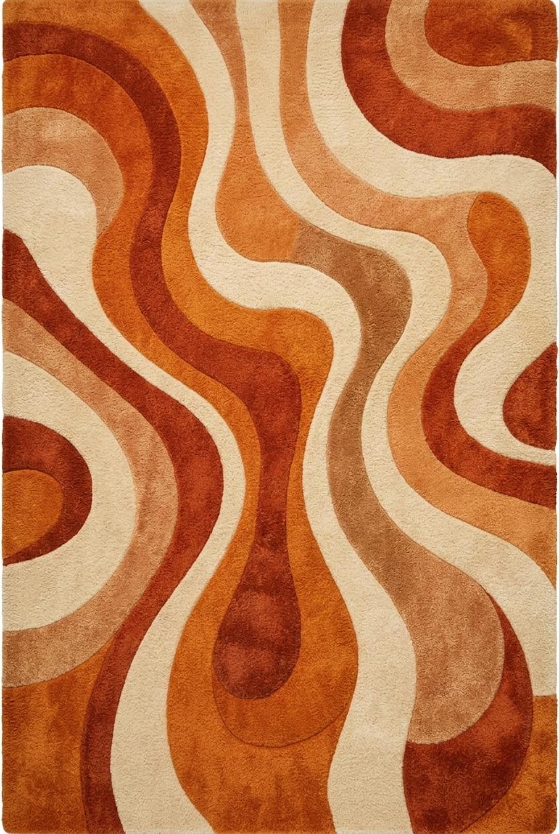 May include: A rectangular rug with a retro design. The rug features a pattern of flowing, wavy lines in shades of orange, brown, and cream. The rug has a soft, textured appearance, suitable for a living room or bedroom.
